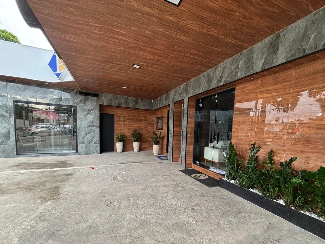 Área de entrada coberta do prédio, com teto em madeira, paredes em mármore cinza e plantas