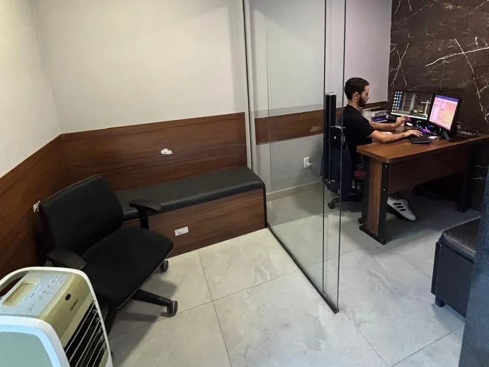 Sala com poltrona e banco estofado ao lado de estação de trabalho com computadores